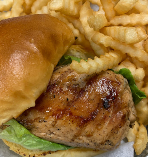 A grilled chicken sandwich with lettuce on a bun, served with a side of crinkle-cut fries.