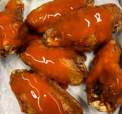 A close-up of crispy chicken wings drizzled with a bright red sauce on a white paper background.