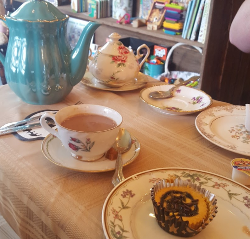 A vintage tea set with a turquoise teapot, teacups, and a cupcake on a table with a patterned tablecloth.
