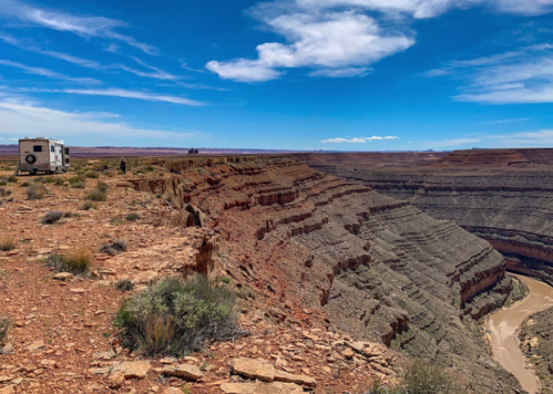 A scenic view of a canyon with layered rock formations and a river below, featuring a camper parked nearby.