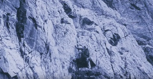 A climber ascends a rugged rock face, showcasing determination and skill in a monochrome setting.