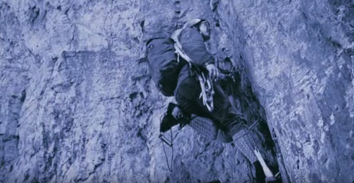 A climber ascends a rocky cliff face, equipped with gear and focused on the challenging ascent.