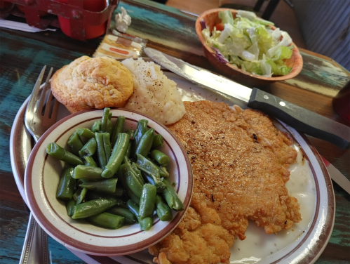 A plate of fried fish, green beans, rice, a muffin, and a small salad on a rustic table.