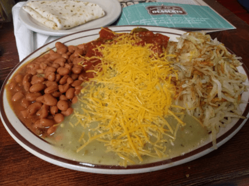 A plate of food featuring refried beans, green sauce with cheese, hash browns, and a side of tortillas.