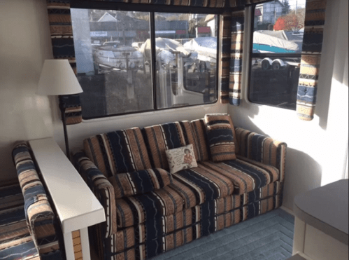 Cozy interior of a recreational vehicle featuring a striped sofa, lamp, and large windows with a view of boats outside.