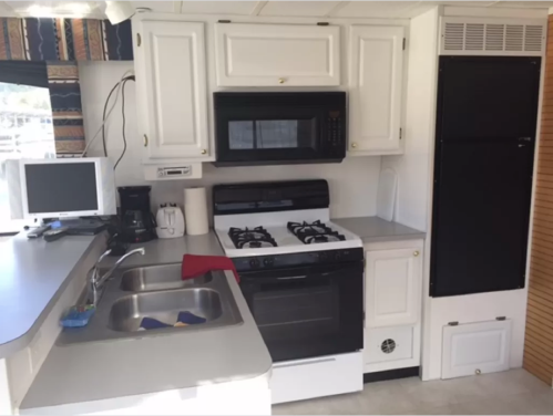 A compact kitchen with white cabinets, a black stove, microwave, sink, and a small refrigerator in a bright space.