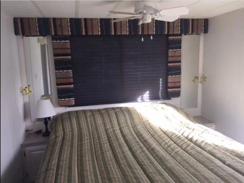 A cozy bedroom with a striped bedspread, a ceiling fan, and a dark window shade above a neatly made bed.
