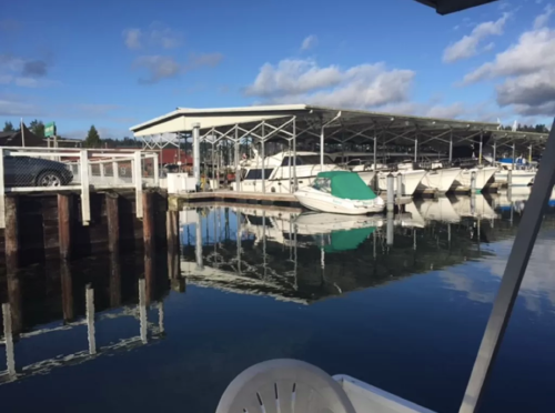 A calm marina scene with boats docked, reflecting in the water under a clear blue sky.
