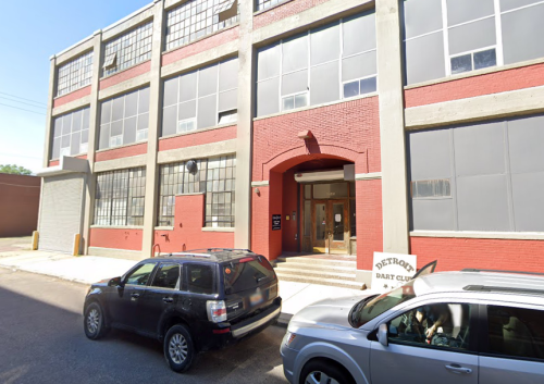 Exterior of the Detroit Dart Club building, featuring large windows and a red brick facade, with parked cars in front.