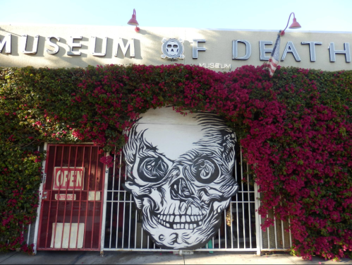 Exterior of the Museum of Death, featuring a large skull mural and vibrant pink flowers on the facade.