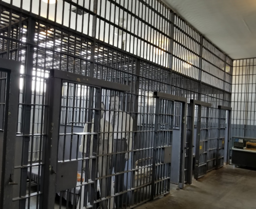 Interior of a prison cell block with multiple barred cells and a concrete floor.