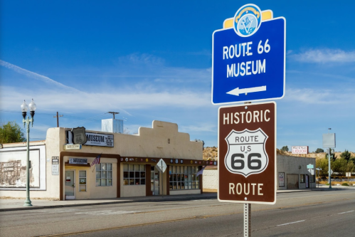 Sign for the Route 66 Museum in front of a historic building, with a clear blue sky in the background.