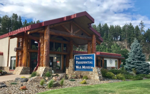 Exterior of the National Presidential Wax Museum, featuring a log cabin-style entrance and landscaped grounds.