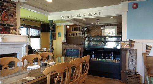 A cozy restaurant interior with wooden tables, a display case, and a wall sign that reads "You are the salt of the earth."