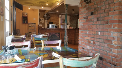 Colorful dining area with wooden tables and chairs, featuring a brick wall and a counter in the background.