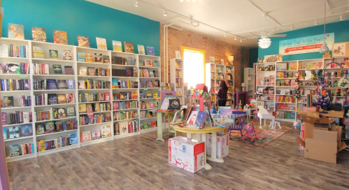 A cozy bookstore interior with colorful shelves filled with books, a reading area, and boxes in the background.