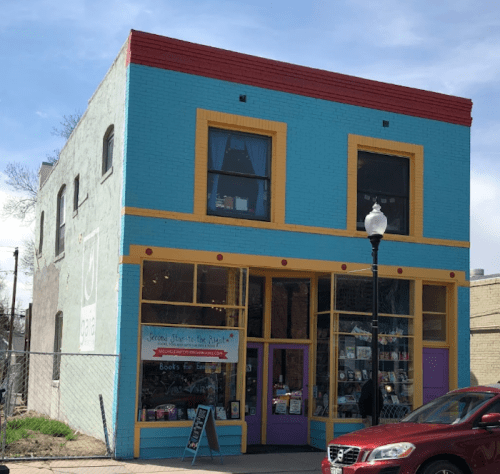 Colorful two-story bookstore with large windows, bright blue and yellow exterior, and a red car parked nearby.