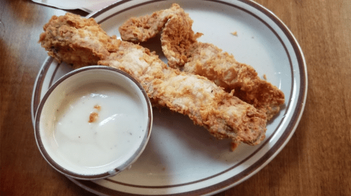 A plate with three pieces of fried chicken and a small bowl of creamy dipping sauce.