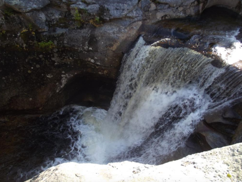 A cascading waterfall flows over rocky terrain, creating white frothy water at the base.