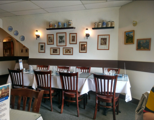 A cozy restaurant interior with a long table set for dining, framed pictures on the walls, and wooden chairs.