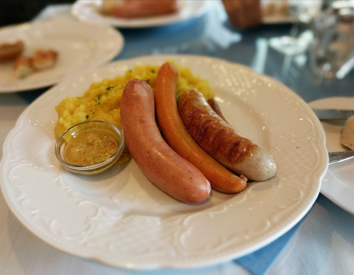 A plate with three types of sausages, mustard, and a serving of mashed potatoes.