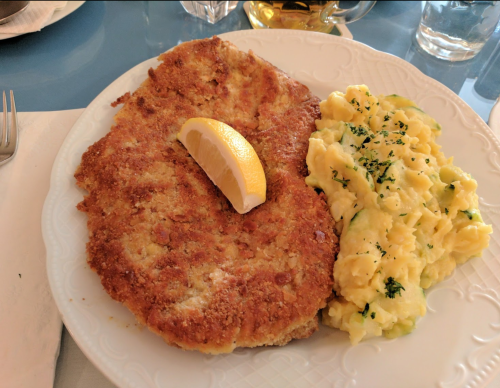 A plate featuring a breaded pork cutlet with a lemon wedge and creamy scrambled eggs garnished with herbs.
