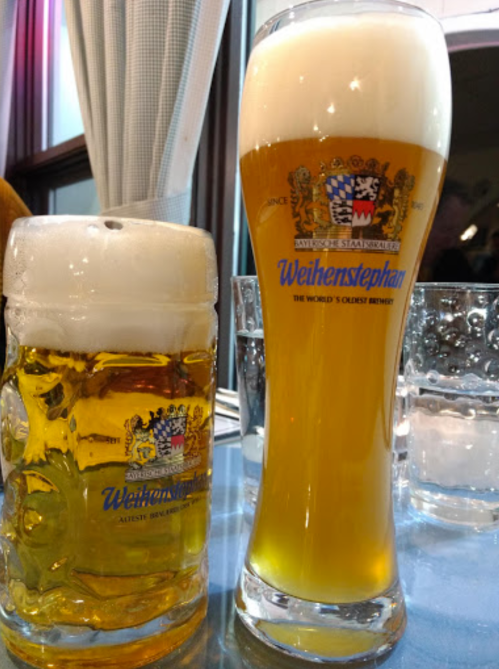 Two glasses of Weihenstephan beer: a tall glass with a frothy top and a smaller mug filled with golden beer.