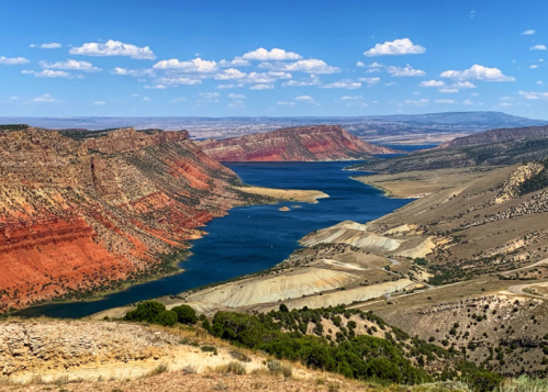 A scenic view of a river winding through colorful cliffs and hills under a blue sky with scattered clouds.