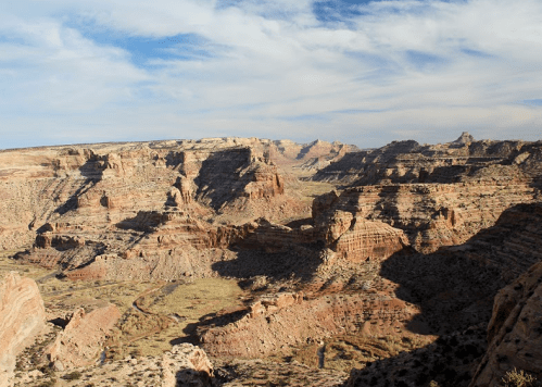 A vast canyon landscape with layered rock formations and a blue sky, showcasing natural beauty and rugged terrain.