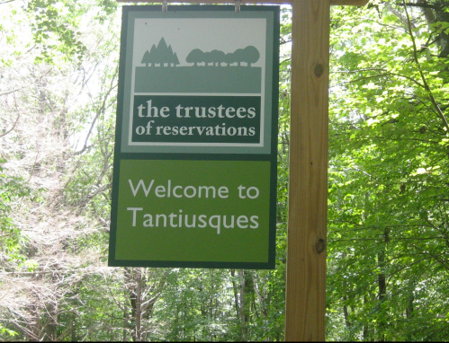 Sign welcoming visitors to Tantiusques, featuring the logo of the Trustees of Reservations, surrounded by trees.