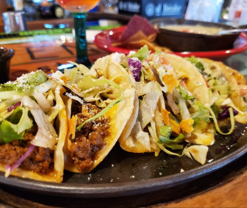 A close-up of a platter featuring several colorful tacos with various toppings, served in a casual dining setting.