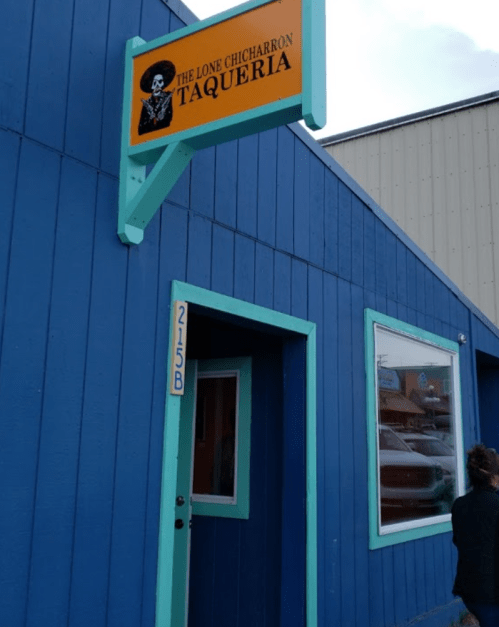 A blue building with a sign reading "The Lone Chicharron Taqueria" and a person standing nearby.
