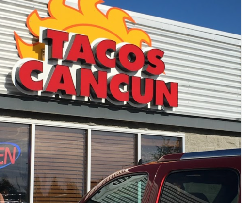 Sign for "Tacos Cancun" with a sun graphic, featuring an "OPEN" neon sign in the window.