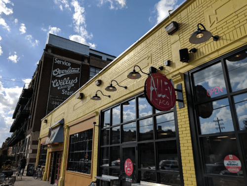 A yellow building with large windows and a sign for "Alley Taco," under a blue sky with scattered clouds.
