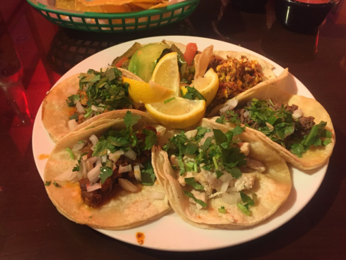 A plate of tacos topped with cilantro and onions, served with lemon wedges and sides of guacamole and rice.