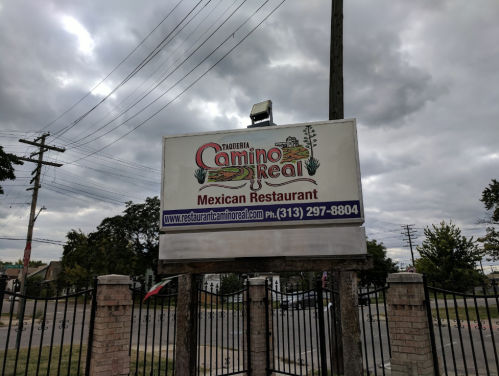Sign for Taqueria Camino Real, a Mexican restaurant, with contact information and cloudy sky in the background.