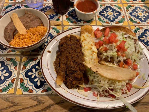 A plate of Mexican food featuring a taco, enchilada, lettuce, tomatoes, and a side of rice and refried beans.