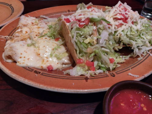 A plate with cheesy enchiladas, a taco filled with lettuce and tomatoes, and a small bowl of salsa.