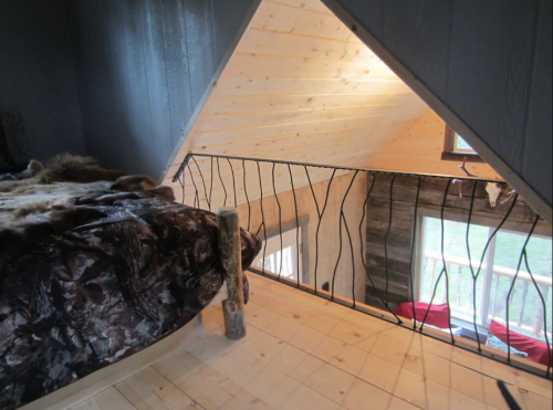 Cozy loft bedroom with wooden walls, a bed, and a railing overlooking a bright, open space below.