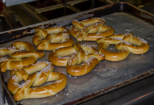 Freshly baked pretzels sprinkled with coarse salt on a metal baking tray.