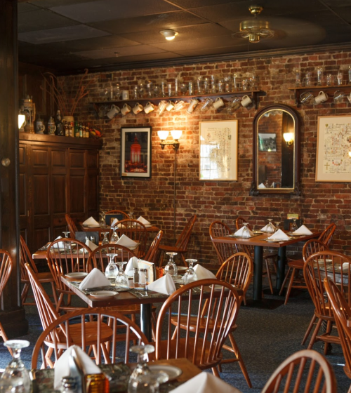 Cozy restaurant interior with wooden tables, chairs, and exposed brick walls, featuring decorative art and soft lighting.