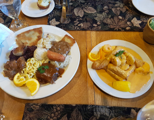 A plate of diverse dishes including meat, rice, vegetables, and a side of sauce, accompanied by a second plate of shrimp.