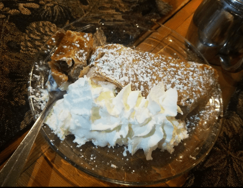 A slice of strudel topped with powdered sugar, served with a dollop of whipped cream on a glass plate.