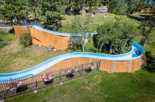 A winding water slide surrounded by greenery and flowers, set in a scenic outdoor area.