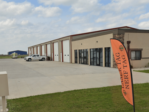 A warehouse with large doors, a truck parked outside, and a flag for "Nerf Tag" in the foreground.