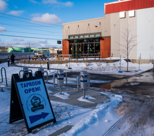 A taproom with a sign reading "Taproom Open," surrounded by snow and outdoor seating.