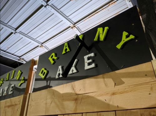Sign with the words "Brainy Bake" in colorful letters, partially obscured by a wooden structure.