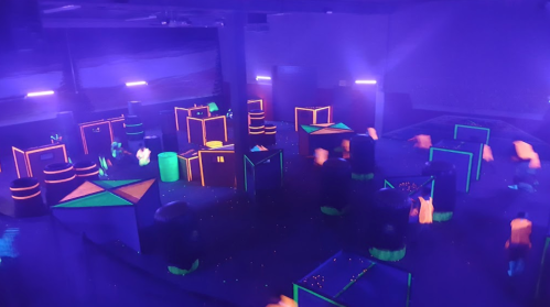 A vibrant indoor laser tag arena with glowing obstacles and neon lights in a dark setting.