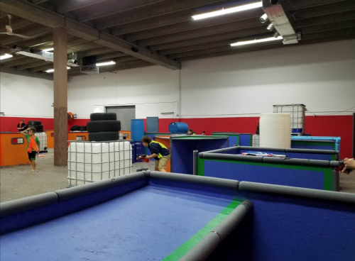 A spacious indoor arena with colorful barriers and players engaged in a game, possibly laser tag or paintball.