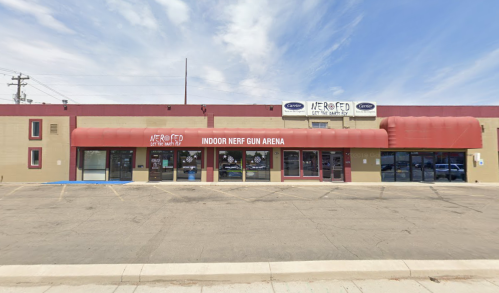 Exterior of an indoor Nerf gun arena with a red awning and large windows, featuring a sign above the entrance.